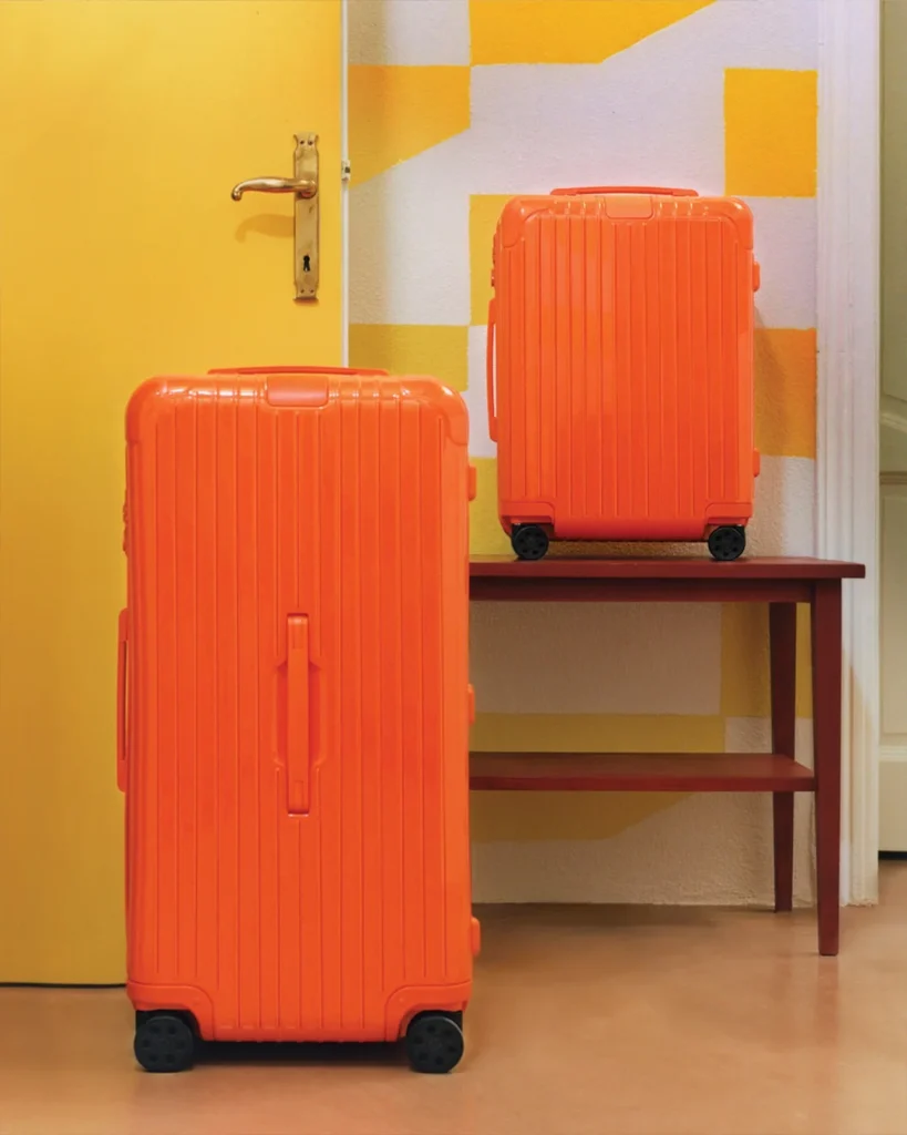 Two orange RIMOWA suitcases in different sizes by the yellow door.