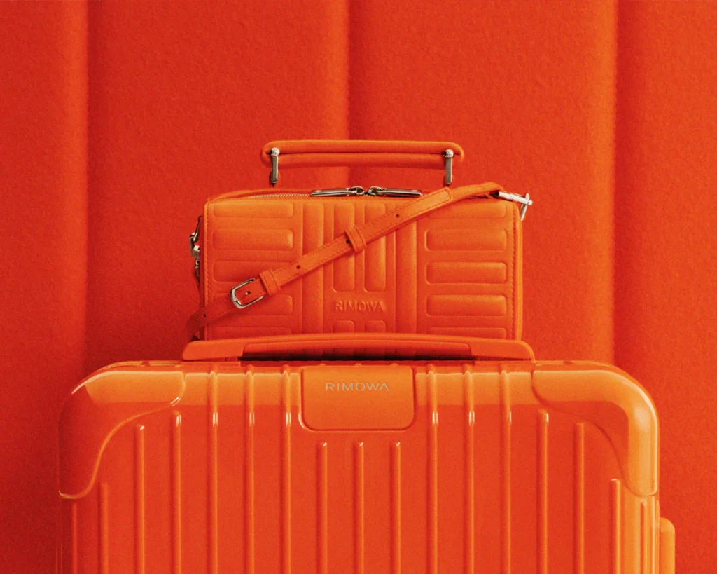 A close-up of an orange RIMOWA Personal mini bag placed on a RIMOWA suitcase in an identical colorway.