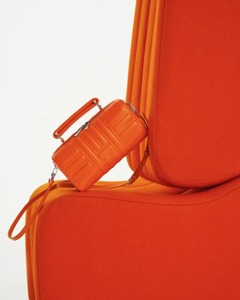 Orange RIMOWA Personal mini bag from the Groove collection on a designer chair.