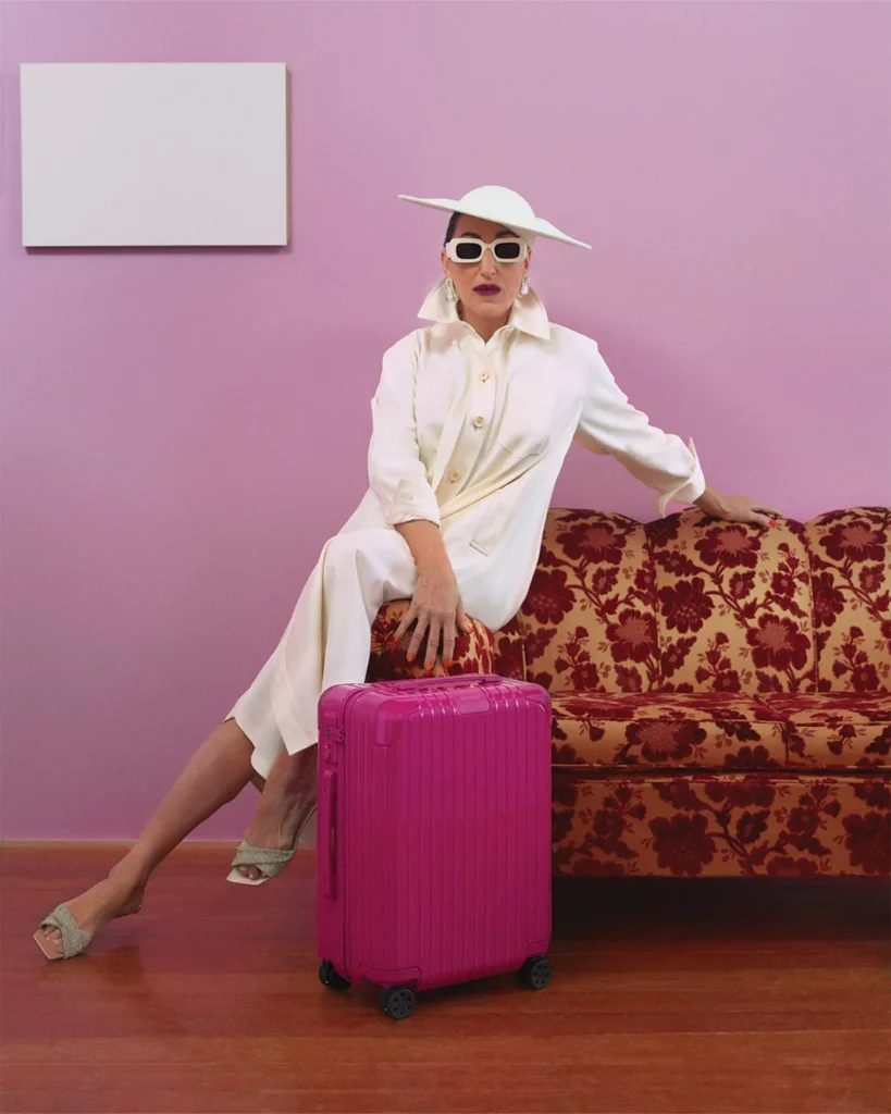 Stylish Rossy de Palma in a white outfit with a magenta RIMOWA suitcase.