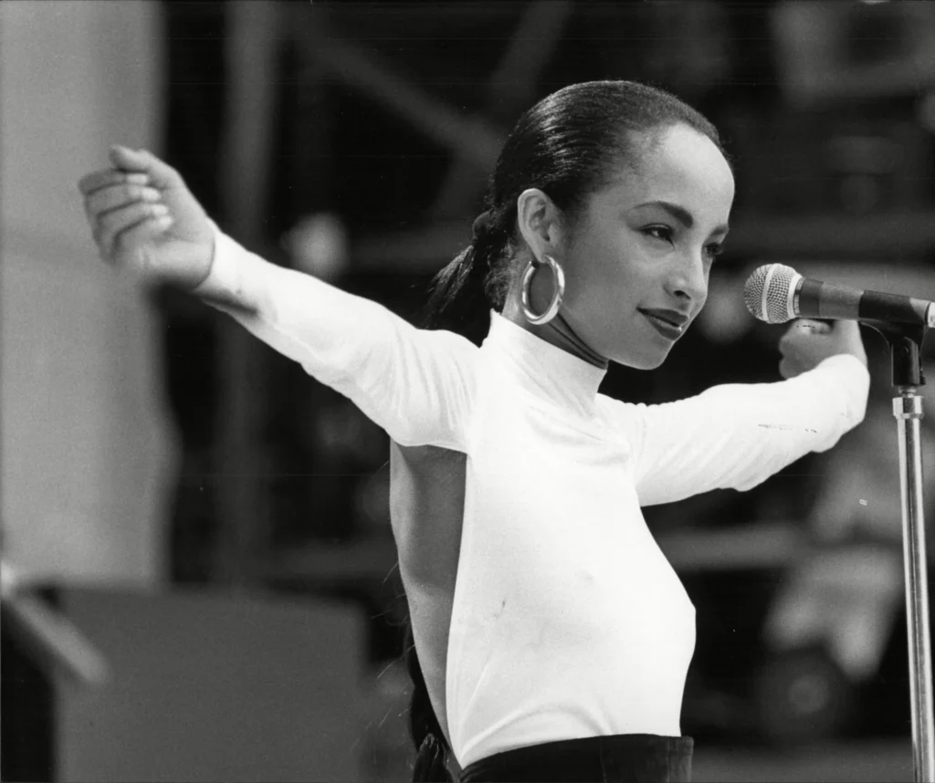 Black and white concert shot of Sade Adu in a backless white top during a performance.