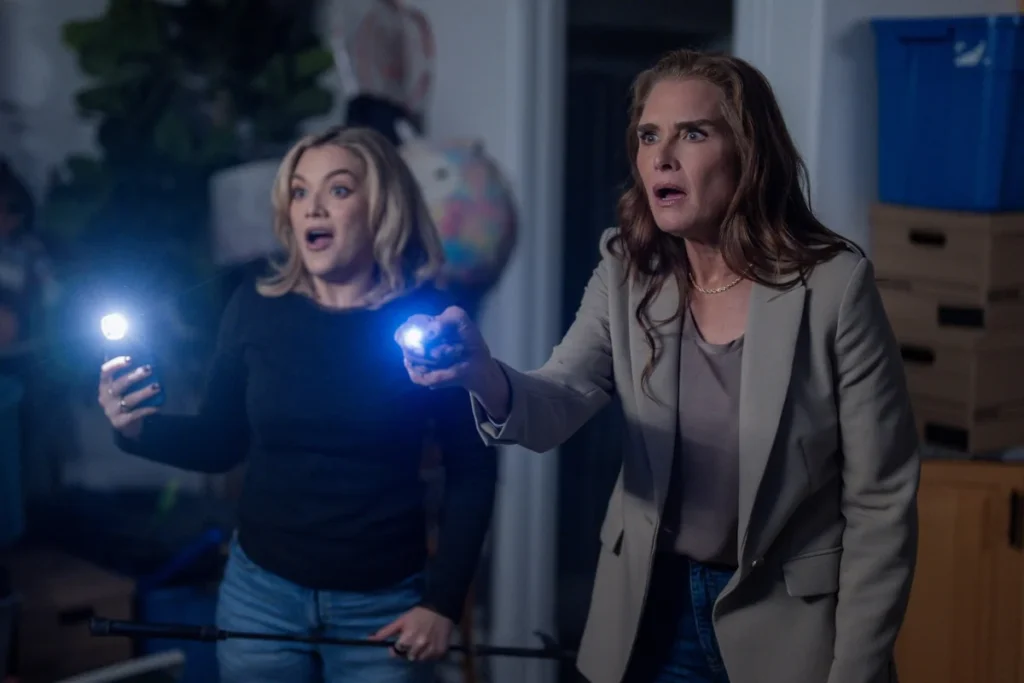 Brooke Shields and Amalia Williamson holding flashlights with shocked expressions during a mystery investigation scene in You're Killing Me.