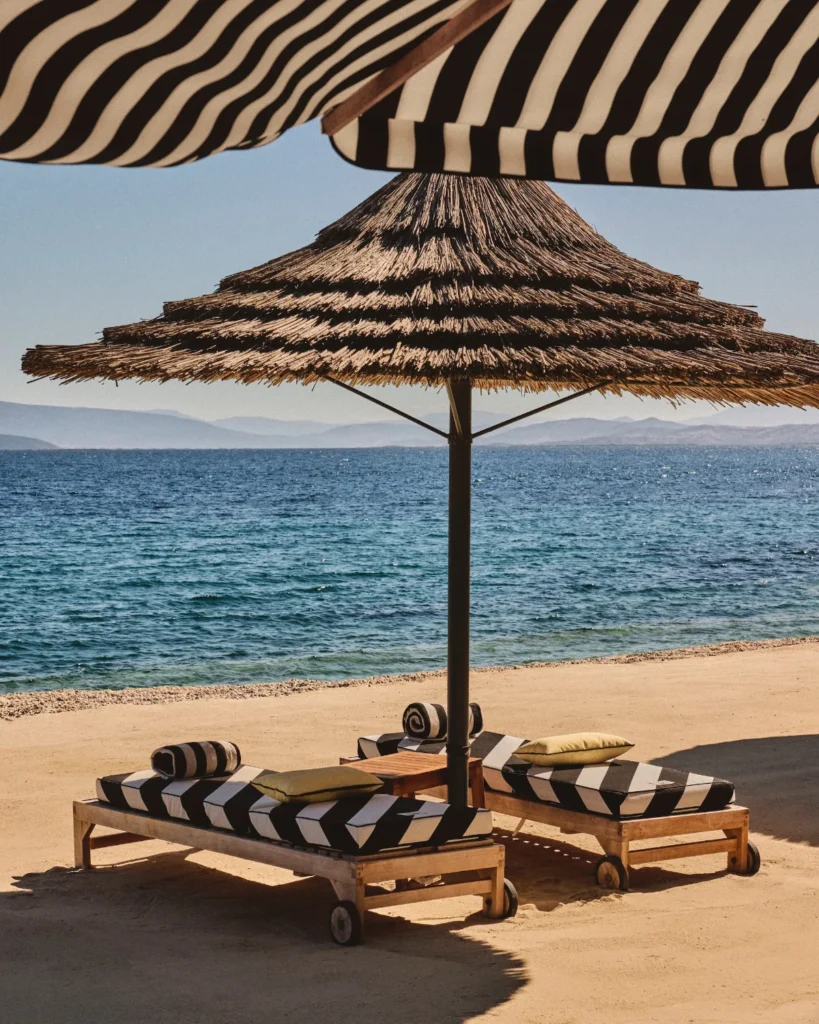 Straw umbrella and beach lounge chairs with a bold black and white striped pattern by designer Jacquemus at the Mandarin Oriental Bodrum resort.