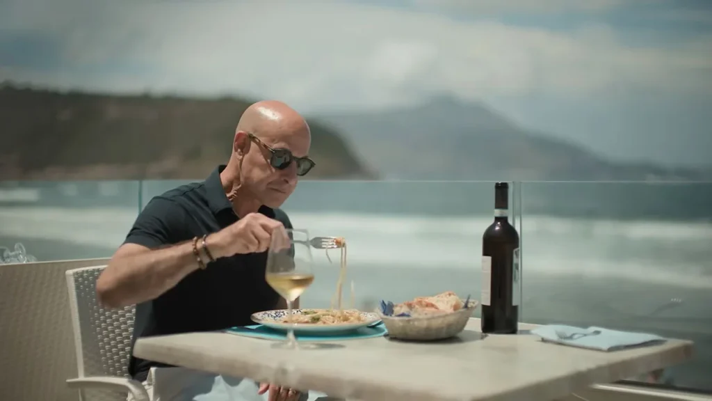 Production still of Stanley Tucci tasting fresh pasta at a seaside terrace from the series.