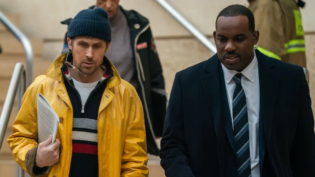 Ryan Gosling in a yellow coat and Lionel Boyce as security officer Carl in Project Hail Mary.