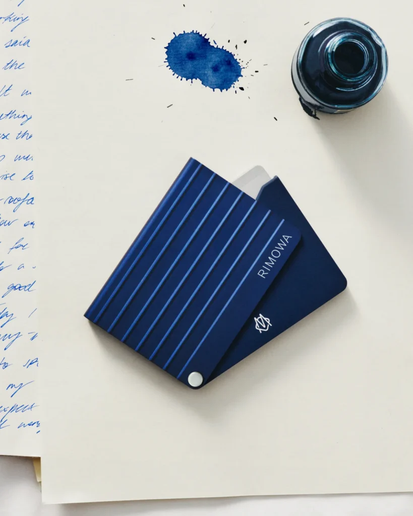 RIMOWA Ink Blue anodised aluminium card holder on handwritten letters with an inkwell.