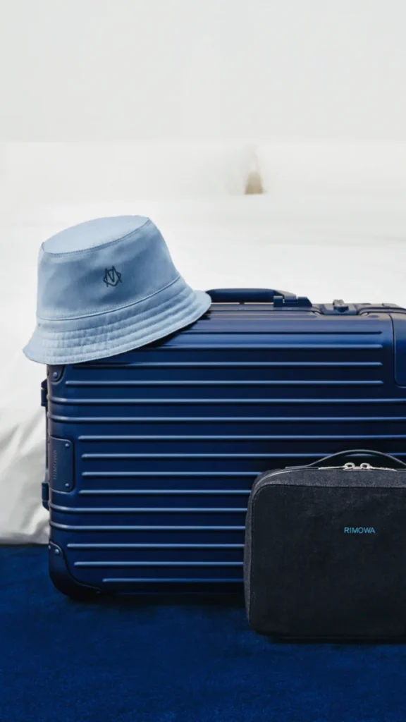 RIMOWA Ink Blue suitcase with a denim bucket hat and toiletry pouch.
