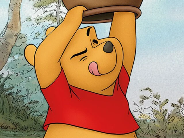 Winnie the Pooh lifts a large honey pot above his head while wearing his signature red shirt.