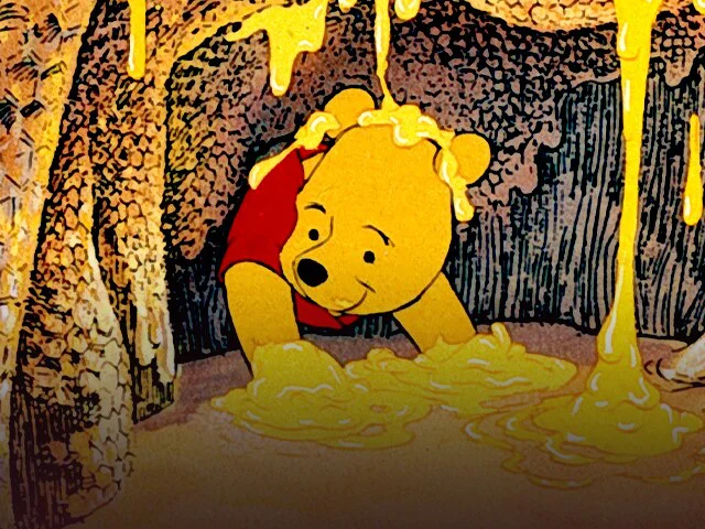 Winnie the Pooh sits inside a hollow tree surrounded by dripping golden honey.